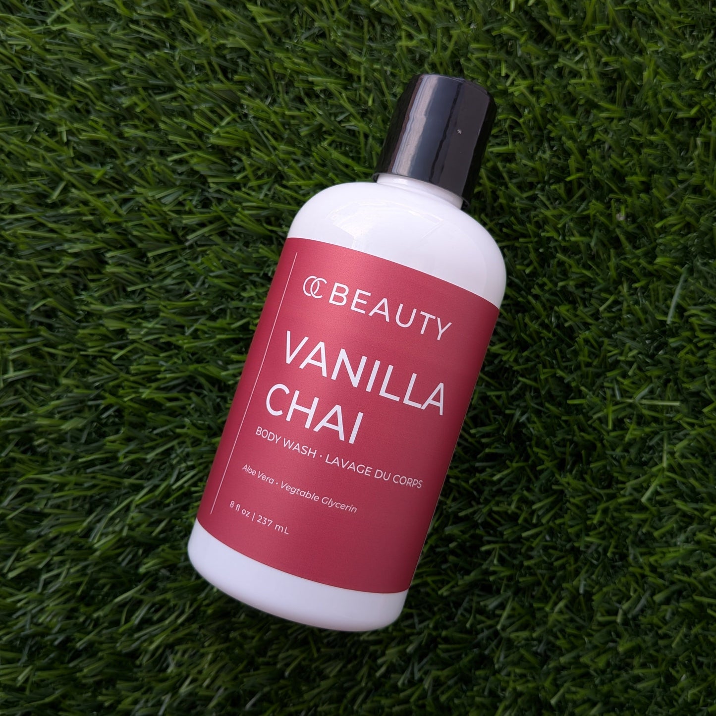 A bottle of OC BEAUTY Vanilla Chai body wash resting diagonally on green grass.