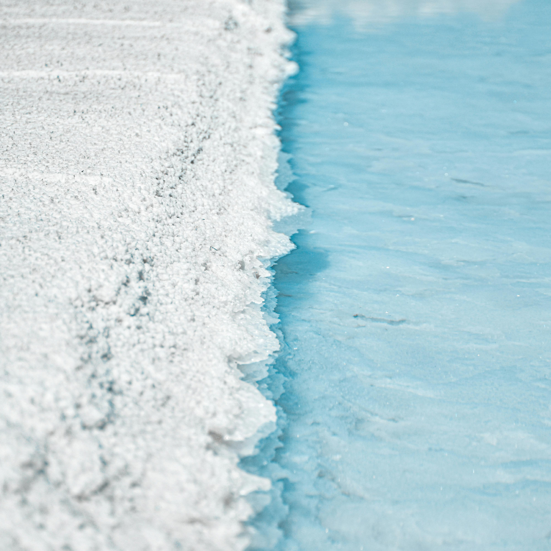 Close-up of a salt crystal formation on a beach with clear blue water.