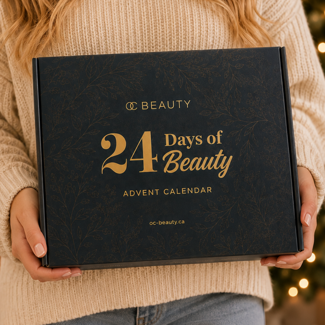 A person in a beige knit sweater holds a black box labeled '24 Days of Beauty Advent Calendar' with gold lettering. The background is softly blurred with warm holiday lights.