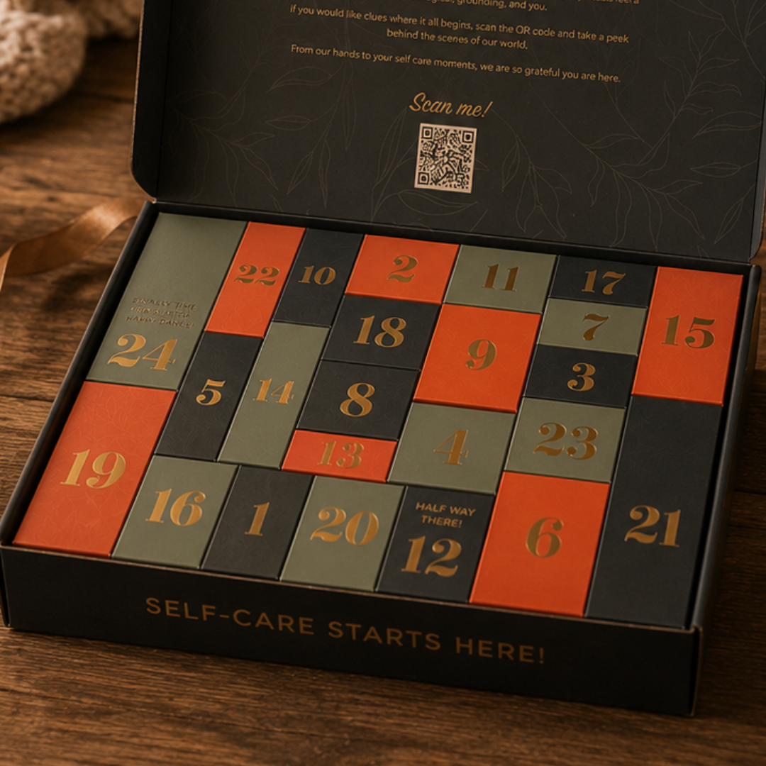 An open Navy blue gift box containing a self-care advent calendar with numbered square boxes in red, green, and navy blue, placed on a wooden surface.