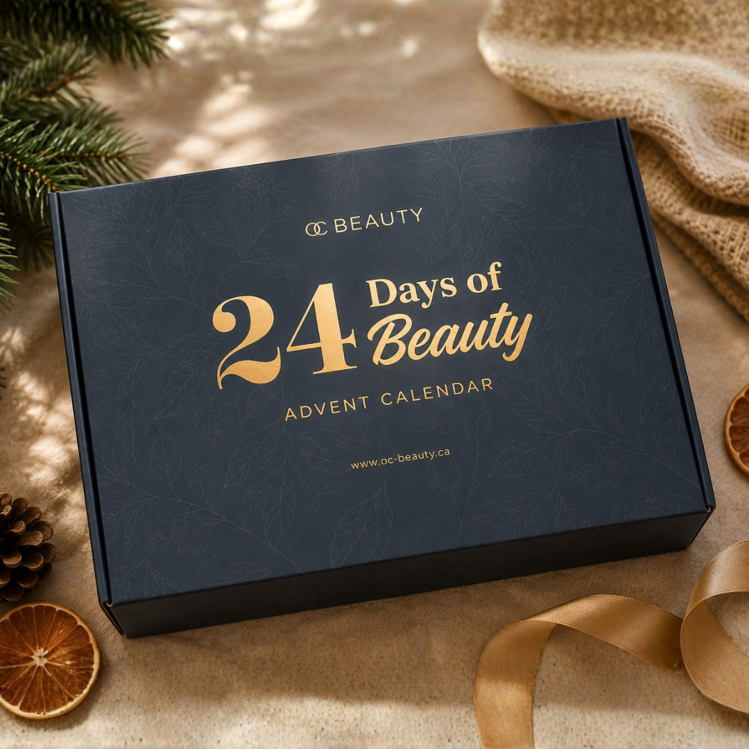 A dark navy blue rectangular box with gold foil text reading '24 Days of Beauty Advent Calendar' and 'OC BEAUTY' at the top, styled on a beige surface with holiday greenery, dried orange slices, a ribbon, and a burlap fabric.