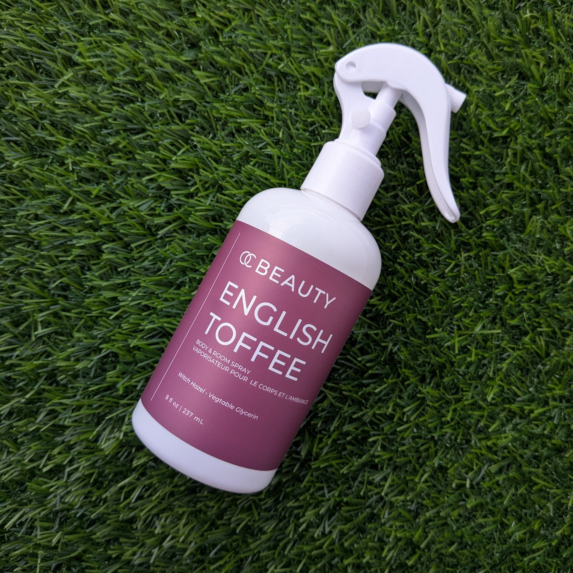 A spray bottle of Beauty English Toffee hair product placed diagonally on green artificial grass.