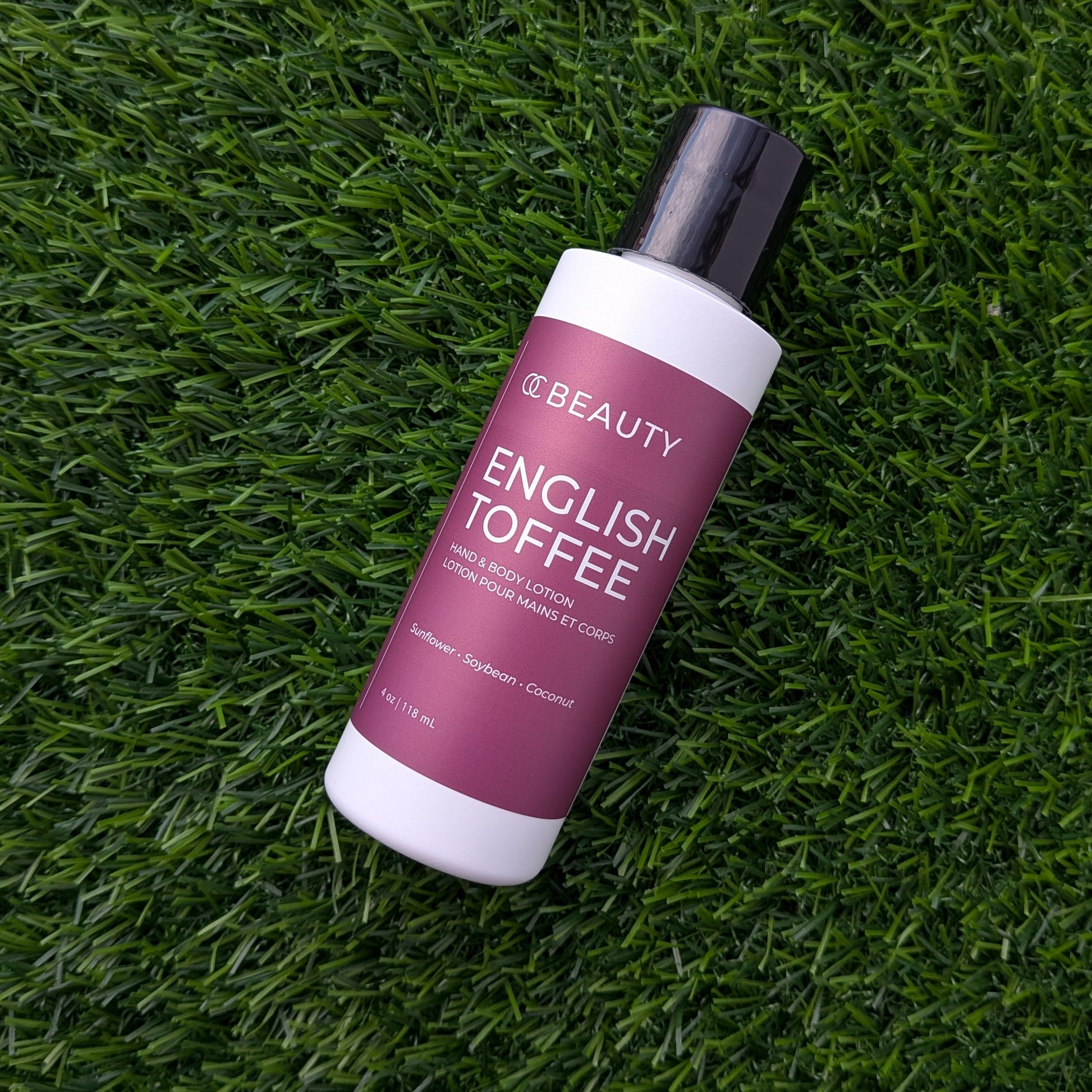 A bottle of BEAUTY English Toffee hair color cream placed diagonally on a textured green grass background.
