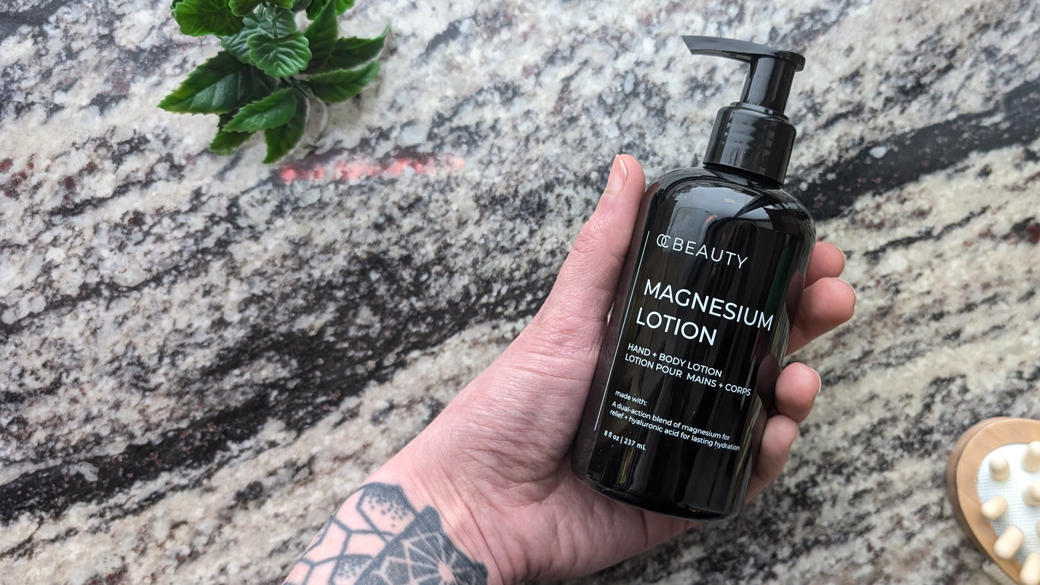 Hand holding a bottle of magnesium lotion on a textured rock surface with a brush and leaves.