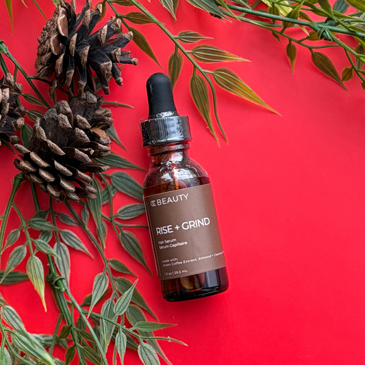 Brown bottle with dropper labeled 'Rise + Grind' on a red background with green leaves and pine cones.