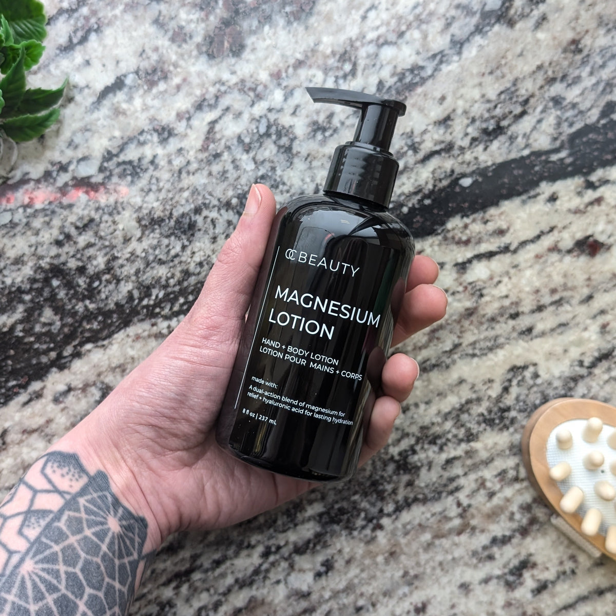 Hand holding a bottle of magnesium lotion on a textured rock surface with a brush and leaves.